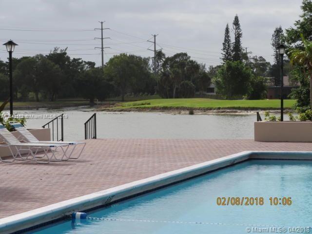 A swimming pool with lounge chairs overlooks a lake and a grassy golf course area — 4170 Inverrary Dr # 111, Lauderhill FL 33319, LAUDERHILL, FL