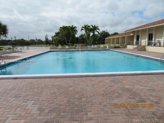 A rectangular swimming pool sits on a brick patio next to a building with palm trees — 4170 Inverrary Dr # 111, Lauderhill FL 33319, LAUDERHILL, FL