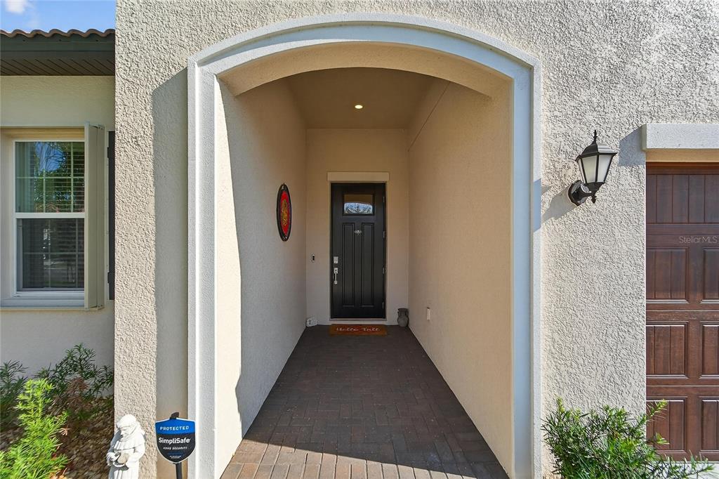 A covered entryway features a dark front door, brick flooring, and a wall-mounted security sign — 17216 SCUBA CREST STREET, WIMAUMA, FL