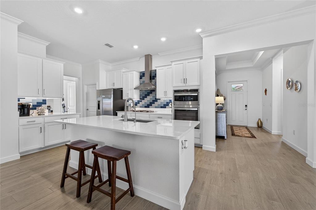 A modern white kitchen features a large island, stainless steel appliances, and blue tile backsplash — 17216 SCUBA CREST STREET, WIMAUMA, FL