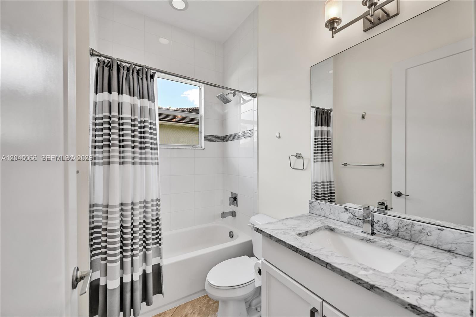 A bathroom features a marble-topped vanity, a white toilet, and a shower-tub combo — 9706 Celtic Sea Ln, Delray Beach FL 33446, DELRAY BEACH, FL