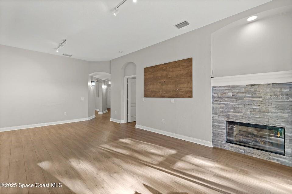 This living room features light wood-look flooring, a stone fireplace, and a wall-mounted wood panel — 1741 KINSALE COURT, MELBOURNE, FL