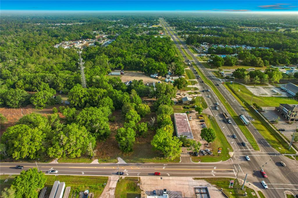 An aerial view shows a wooded lot adjacent to a multi-lane highway and commercial buildings — 1301, 1225, 1215 DUFF RD, LAKELAND, FL