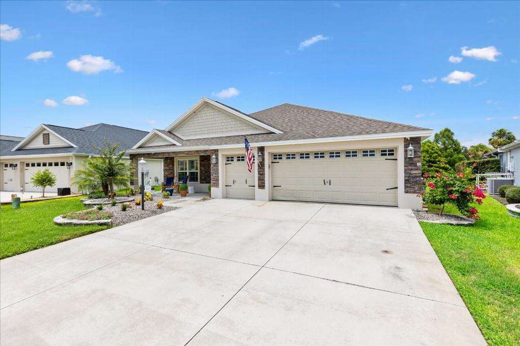 A single-story suburban house with a stone facade, a three-car garage, and a concrete driveway — 5581 PASSION FLOWER WAY, THE VILLAGES, FL