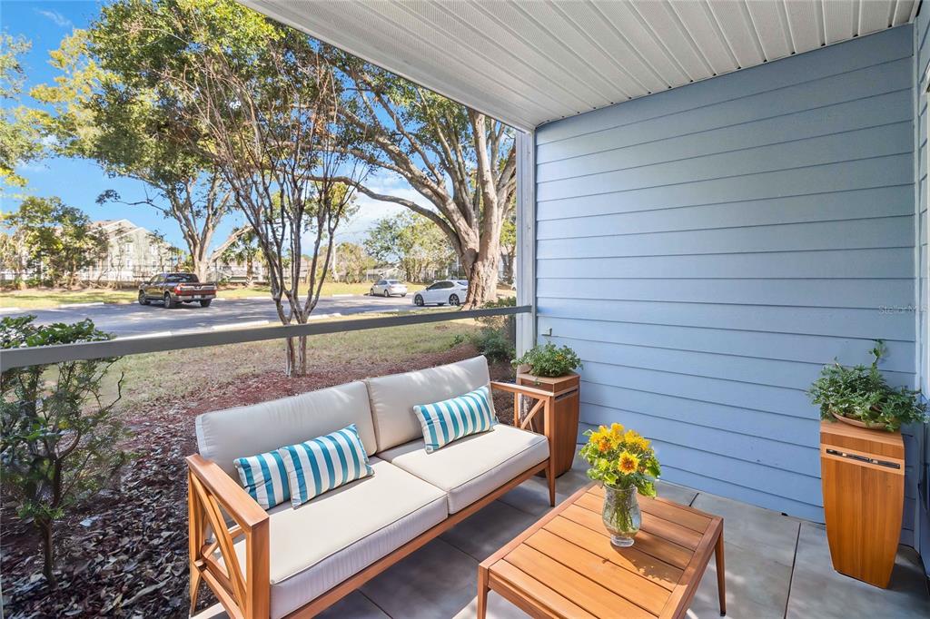 A covered patio features a wooden loveseat, a matching coffee table, and two potted plants — 731 SUGAR BAY WAY UNIT 103, LAKE MARY, FL