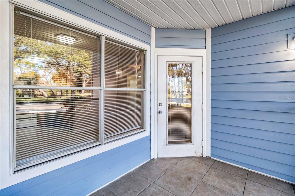 A covered patio with blue horizontal siding, a glass-paneled door, and a large window — 731 SUGAR BAY WAY UNIT 103, LAKE MARY, FL
