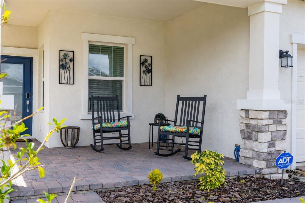 A covered front porch features two black rocking chairs, a small side table, and stone accents — 4536 OCHOS RIOS PLACE, KISSIMMEE, FL