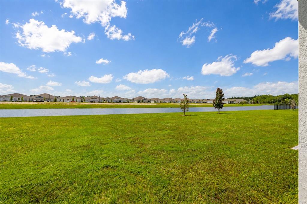 A grassy backyard overlooks a pond with a row of houses in the distance — 4536 OCHOS RIOS PLACE, KISSIMMEE, FL