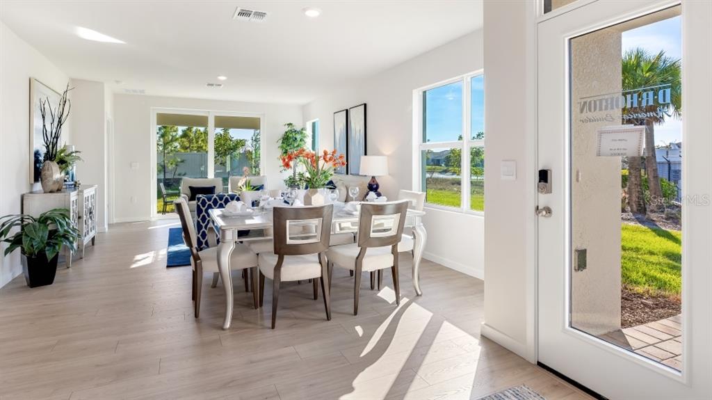 A bright dining room features a table with six chairs, light wood flooring, and windows — 1609 INDIAN GRASS PLACE, PARRISH, FL