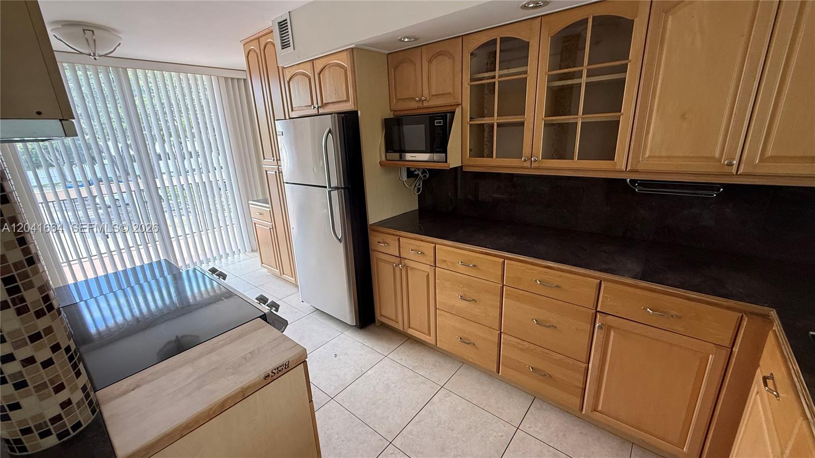 A kitchen features light wood cabinets, black countertops, stainless steel appliances, and tile flooring — 2921 SW 87th Ave # 511, Davie FL 33328, DAVIE, FL