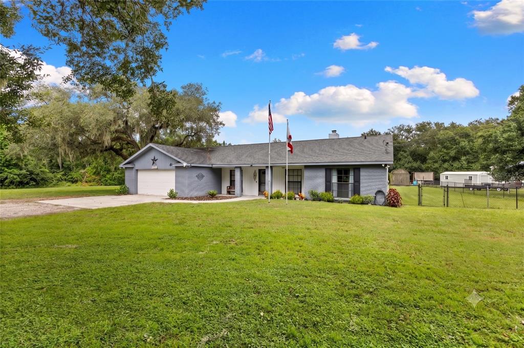 A single-story gray brick house with a two-car garage and two flagpoles in front — 4605 POST HOUSE DRIVE, PLANT CITY, FL