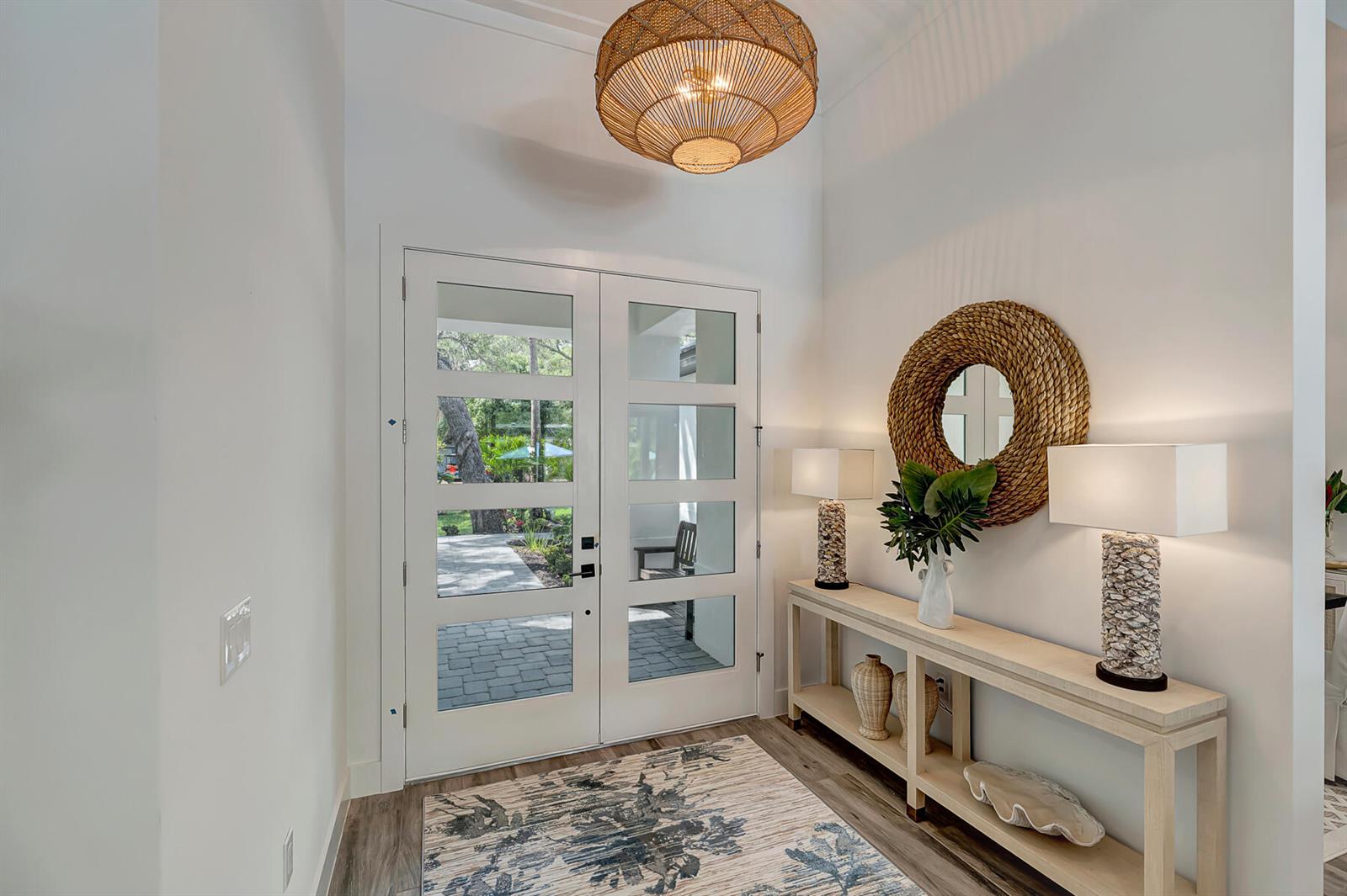 A bright entryway features a double glass door, a console table, and a woven chandelier — VERO BEACH, FL