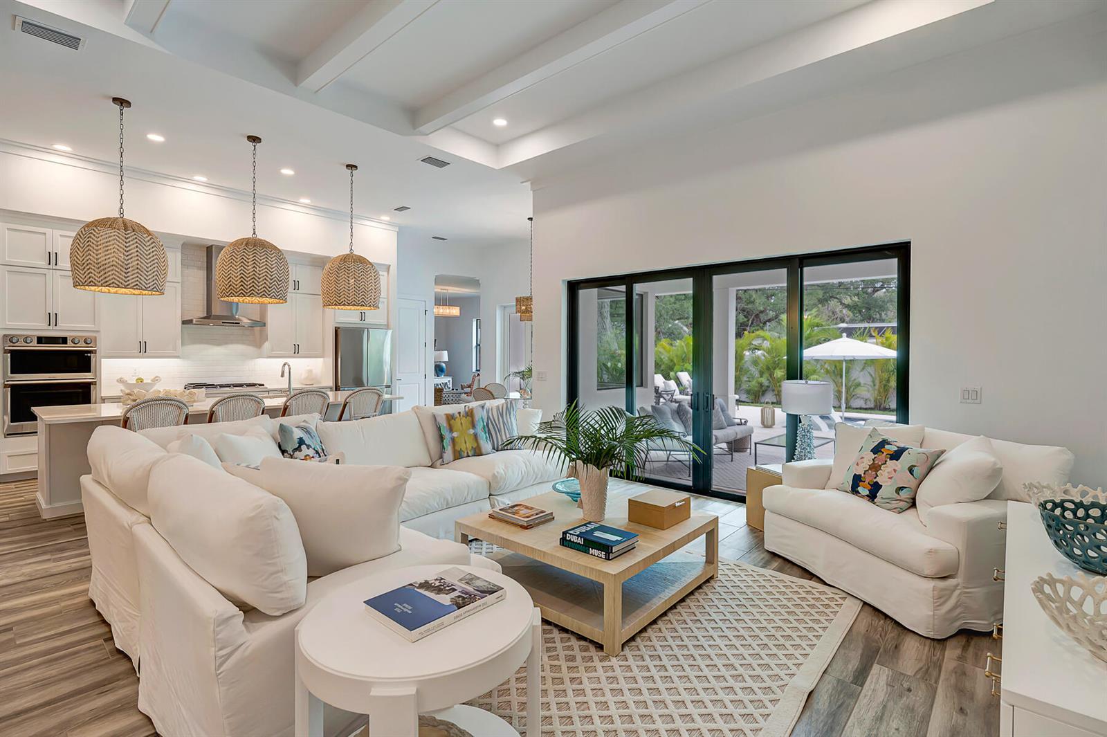 A bright open-concept living room features white sofas, a wooden coffee table, and sliding doors — VERO BEACH, FL