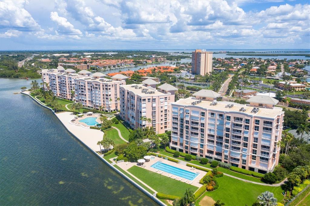 An aerial view shows waterfront apartment buildings with swimming pools and landscaped grounds — 4993 BACOPA LANE S UNIT 705, ST PETERSBURG, FL