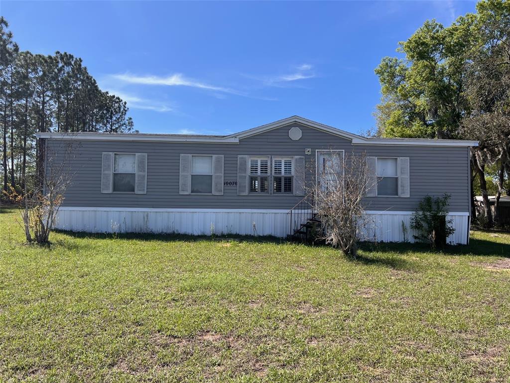 A single-story manufactured home with grey vinyl siding and a white skirting sits on grass — 10070 S ARABIAN AVENUE, FLORAL CITY, FL
