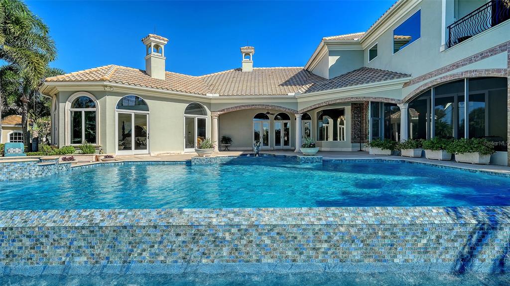 A large swimming pool sits in front of a two-story house with a tiled roof — 7320 BARCLAY COURT, UNIVERSITY PARK, FL