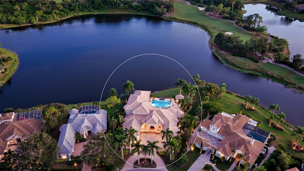 An aerial view shows a large house with a pool, surrounded by a lake and golf course — 7320 BARCLAY COURT, UNIVERSITY PARK, FL