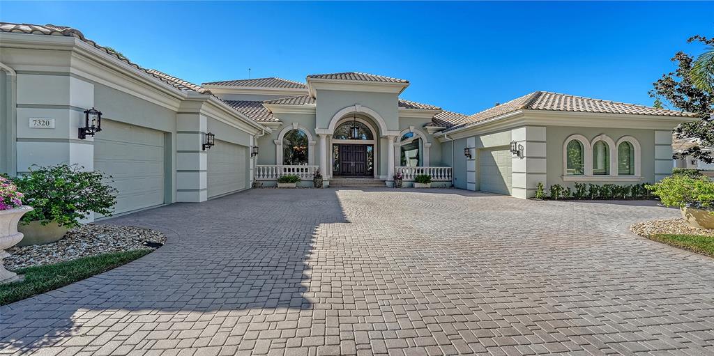 A large, light-colored house features a paved driveway, arched windows, and a tiled roof — 7320 BARCLAY COURT, UNIVERSITY PARK, FL