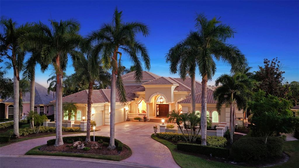 A large, single-story Mediterranean-style house with a paved driveway and palm trees at dusk — 7320 BARCLAY COURT, UNIVERSITY PARK, FL