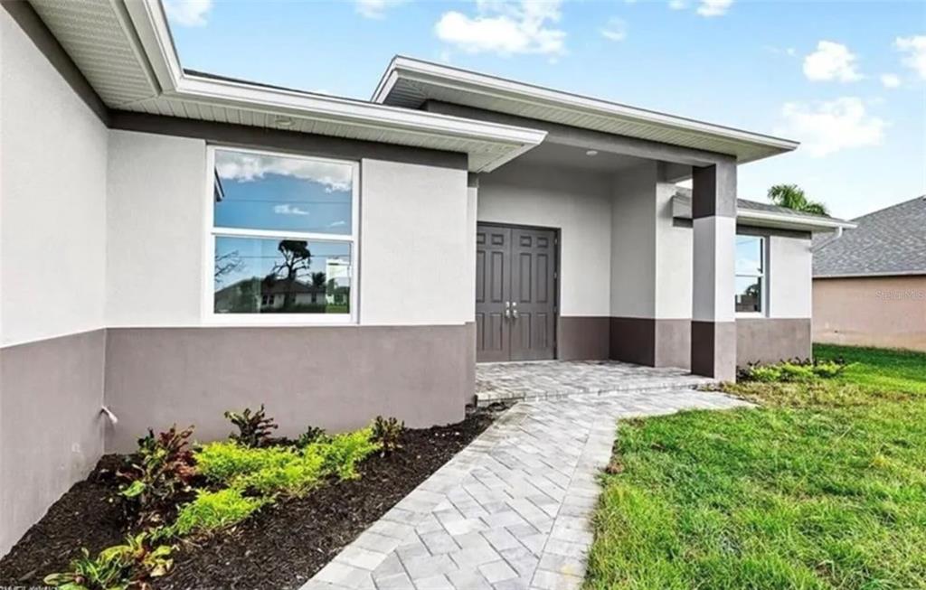 A paved walkway leads to the front entrance of a house with gray and white siding — 928 NE 3RD AVENUE, CAPE CORAL, FL