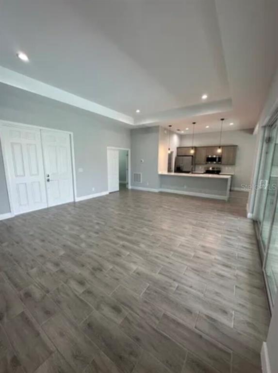 An open-concept living area features light gray walls, wood-look tile flooring, and a modern kitchen — 928 NE 3RD AVENUE, CAPE CORAL, FL