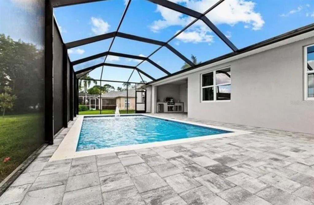 A screened-in patio features a rectangular swimming pool, paver flooring, and an outdoor kitchen area — 928 NE 3RD AVENUE, CAPE CORAL, FL