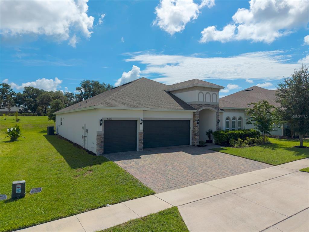 A single-story house with a three-car garage, stone accents, and a paved driveway — 600 AVILA PLACE, HOWEY IN THE HILLS, FL