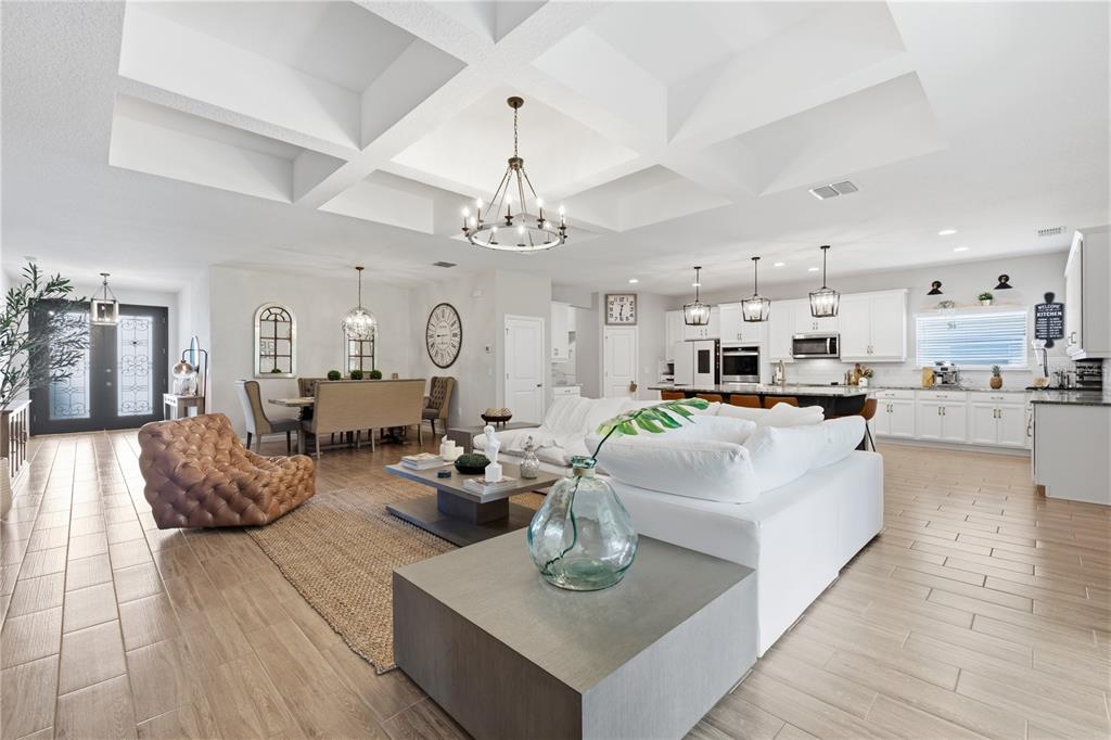 An open-concept living room and kitchen featuring a coffered ceiling and light wood-look flooring — 600 AVILA PLACE, HOWEY IN THE HILLS, FL