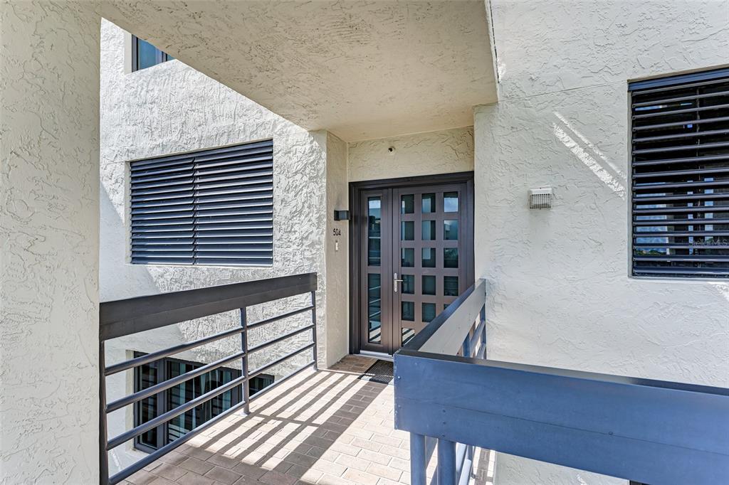 An exterior view of a building entrance with a dark double door and balcony railings — 1135 GULF OF MEXICO DRIVE UNIT 504, LONGBOAT KEY, FL