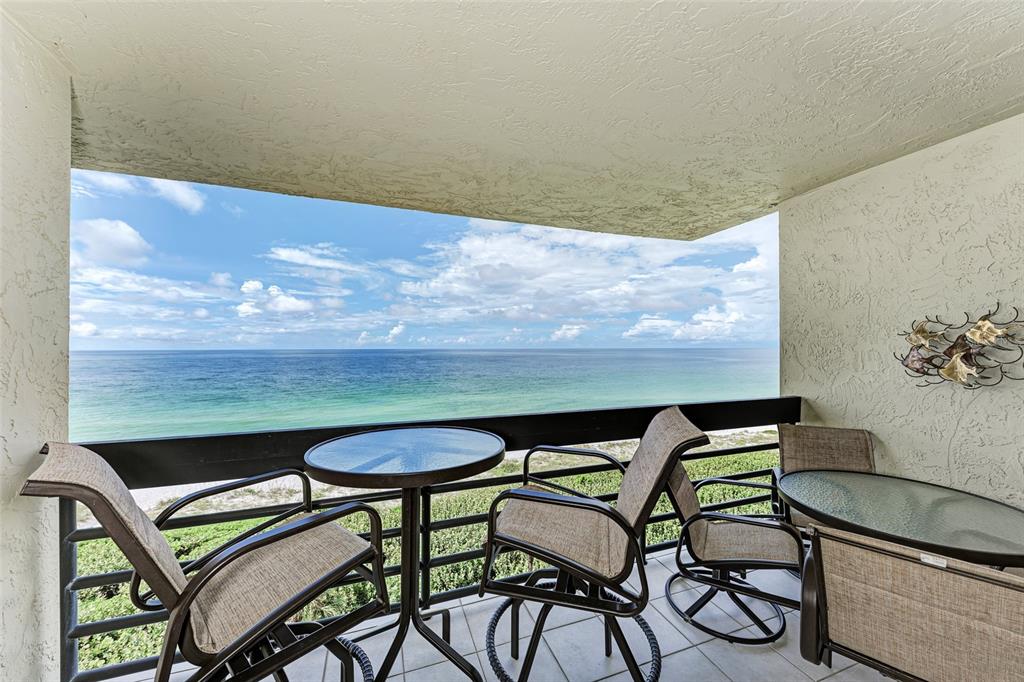 A balcony with patio furniture overlooks the ocean under a blue sky with white clouds — 1135 GULF OF MEXICO DRIVE UNIT 504, LONGBOAT KEY, FL