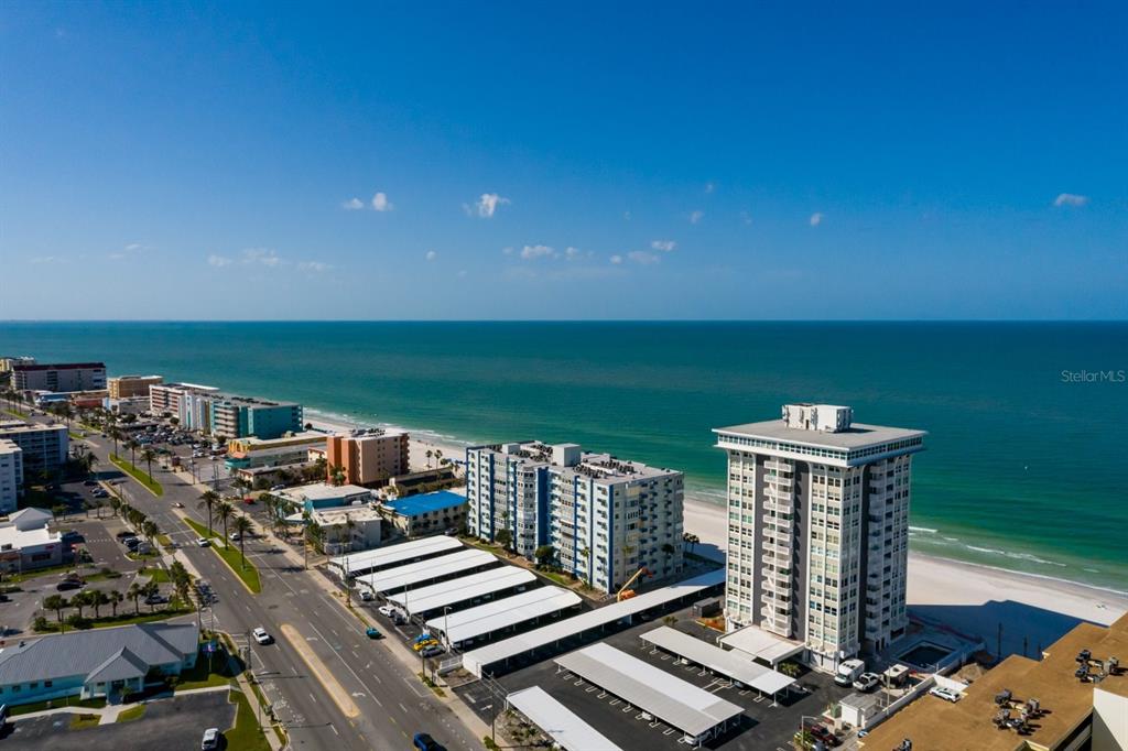An aerial view of a coastal beach town featuring high-rise buildings, parking lots, and oceanfront — 17408 GULF BOULEVARD UNIT 203, REDINGTON SHORES, FL