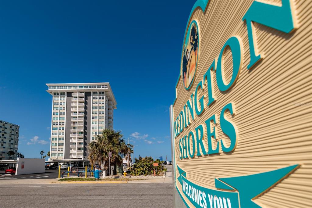 A sign welcoming visitors to Redington Shores stands before a tall, multi-story beachside apartment building — 17408 GULF BOULEVARD UNIT 203, REDINGTON SHORES, FL