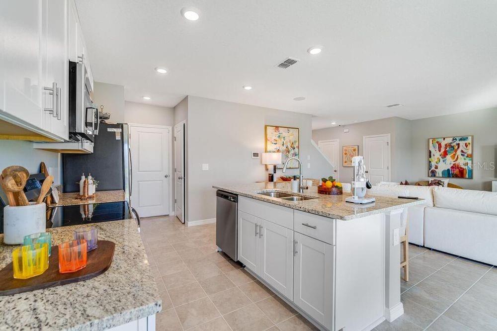 A kitchen with white cabinets, granite countertops, and a central island overlooking a living area — 12422 WHISK COURT, HUDSON, FL