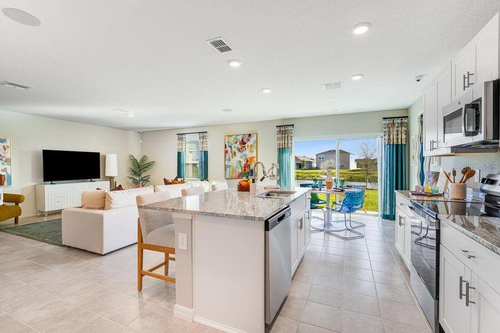 An open-concept kitchen with granite countertops and a large island overlooks a living area — 12422 WHISK COURT, HUDSON, FL