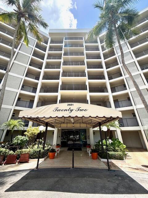 A low-angle view of a multi-story apartment building with a beige awning over the entrance — 2681 S Course Drive # 712, Pompano Beach FL 33069, POMPANO BEACH, FL