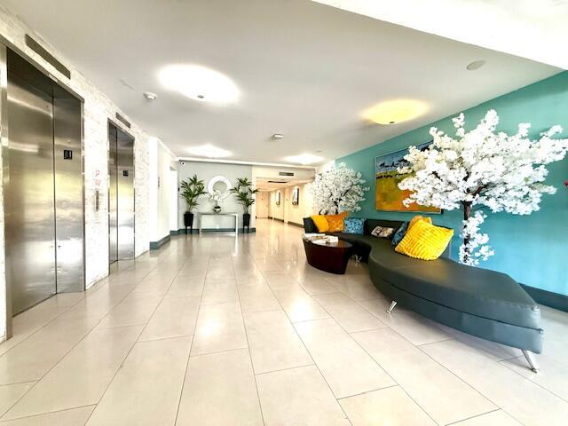 A modern building lobby features stainless steel elevators, tile flooring, and a curved lounge sofa — 2681 S Course Drive # 712, Pompano Beach FL 33069, POMPANO BEACH, FL