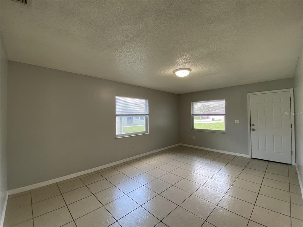 An empty room features light gray walls, beige tile flooring, two windows, and a white door — 118 EATON STREET UNIT 4, EATONVILLE, FL