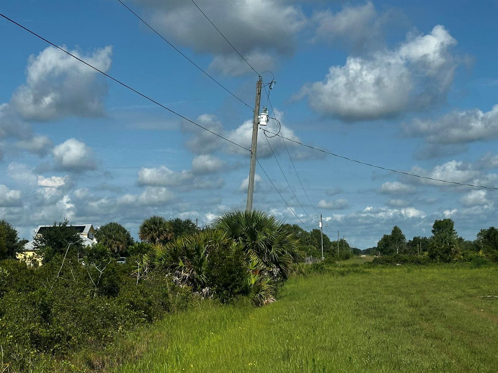 A utility pole with a transformer stands in a grassy field under a cloudy sky — 15138 NW 262nd Street, Okeechobee FL 34972, OKEECHOBEE, FL