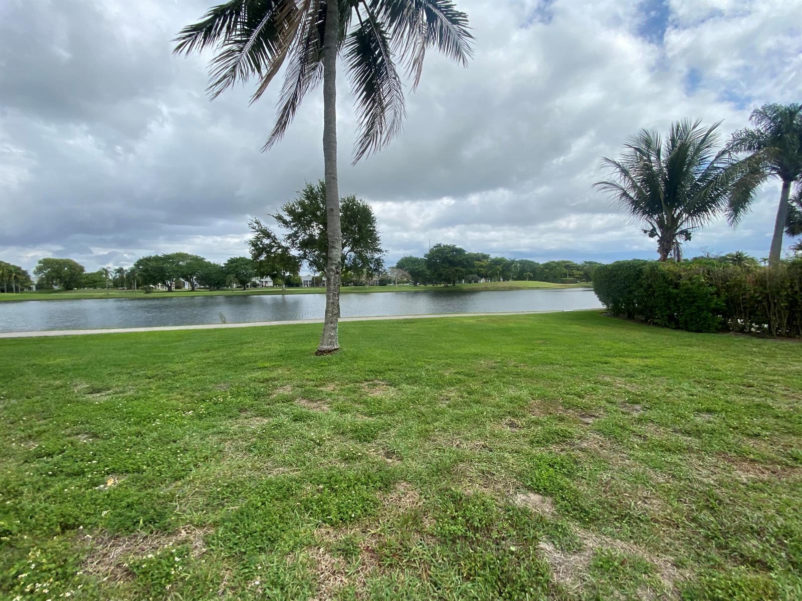 A grassy yard with a palm tree overlooks a lake under a cloudy sky — 62 Willow Circle, Boynton Beach FL 33436, BOYNTON BEACH, FL