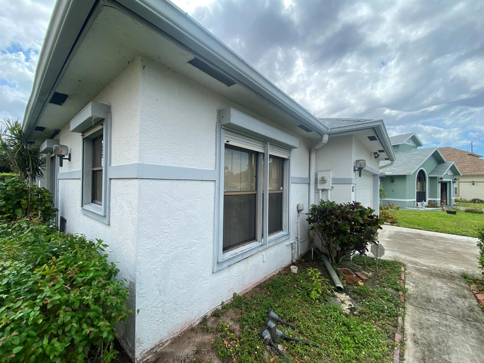 A white stucco house exterior features gray trim, window shutters, and a concrete driveway — 62 Willow Circle, Boynton Beach FL 33436, BOYNTON BEACH, FL