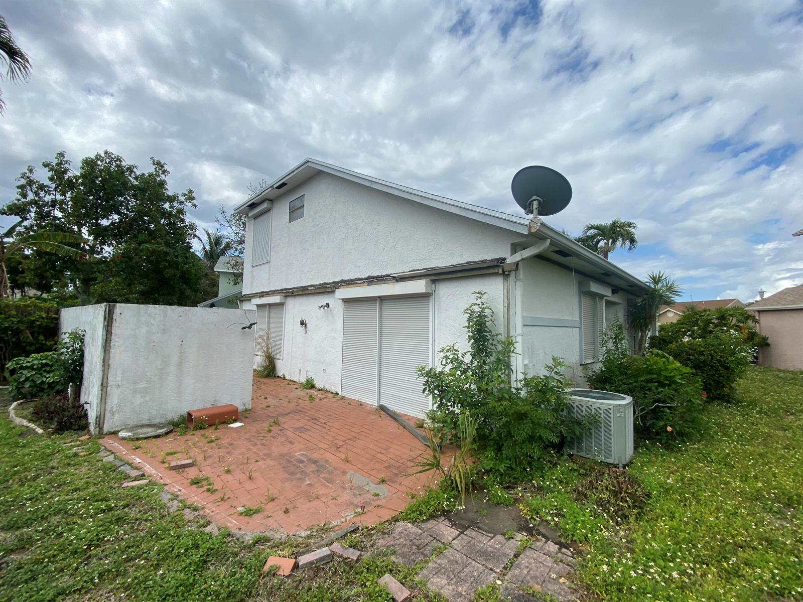 The exterior of a two-story white house features a brick patio and metal storm shutters — 62 Willow Circle, Boynton Beach FL 33436, BOYNTON BEACH, FL