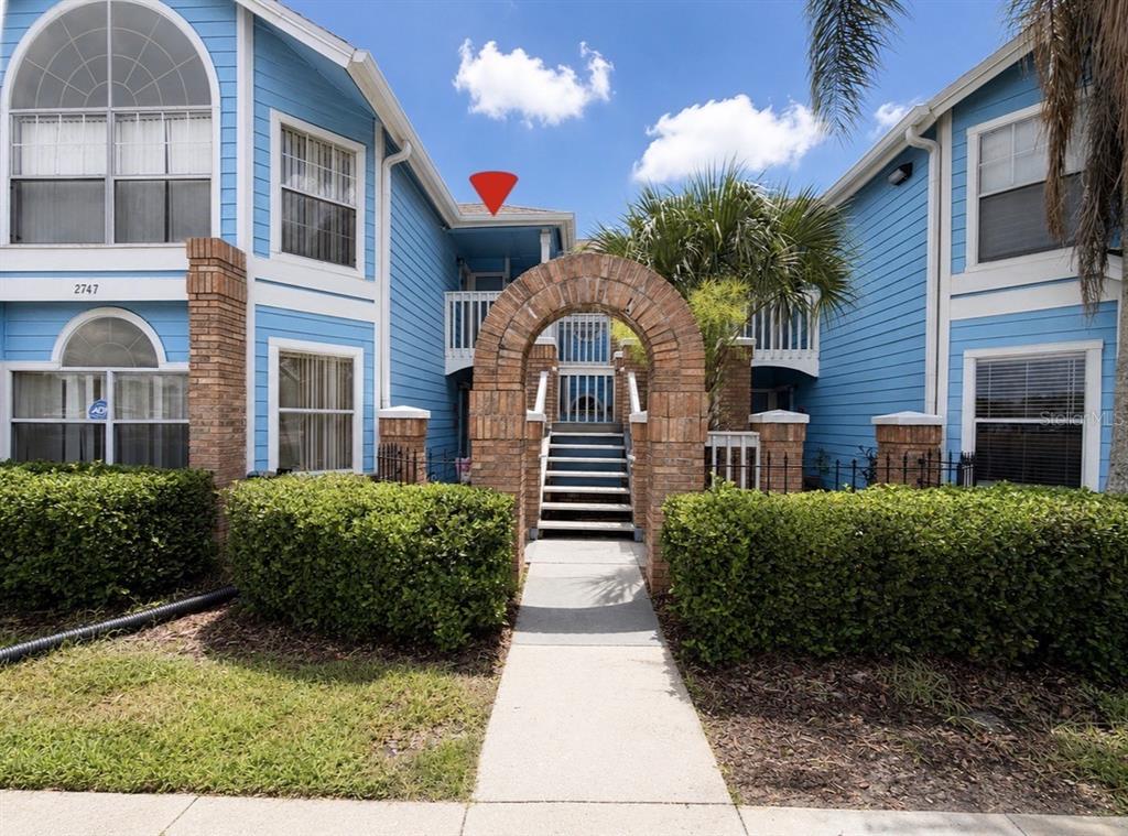 A blue two-story apartment building features a brick archway leading to a central staircase — 2747 N POINCIANA BOULEVARD UNIT 10, KISSIMMEE, FL