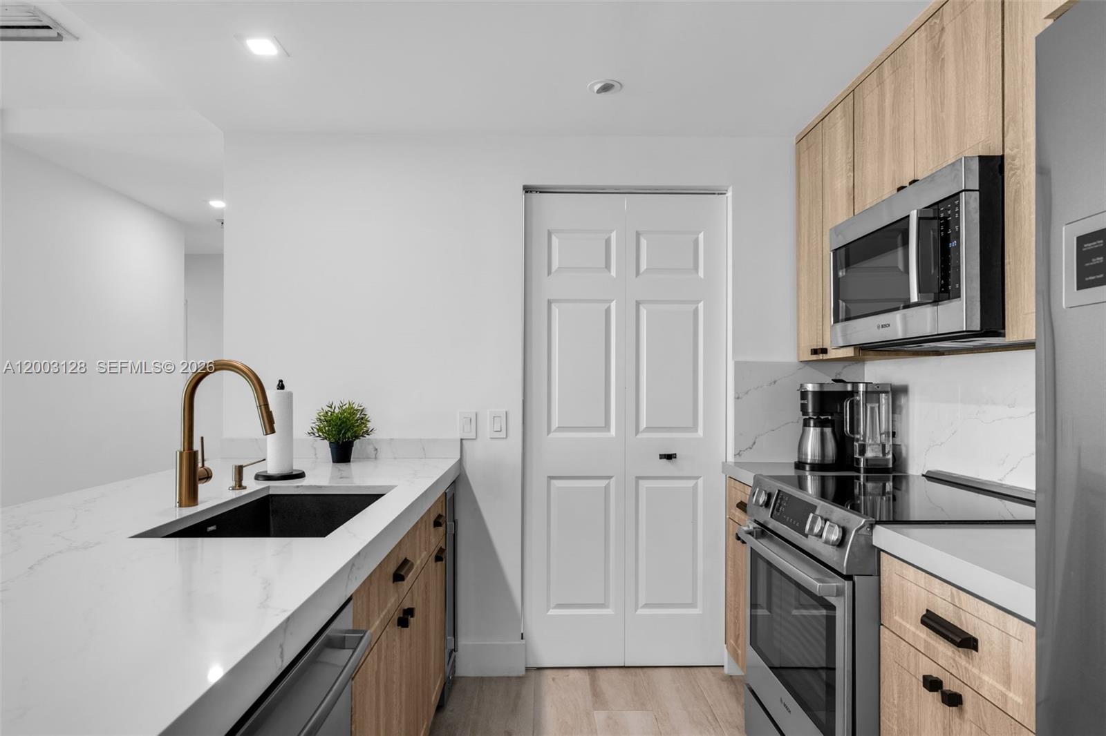 A modern kitchen features light wood cabinets, white countertops, a black sink, and stainless appliances — 1300 Ponce De Leon Blvd # 815, Coral Gables FL 33134, CORAL GABLES, FL