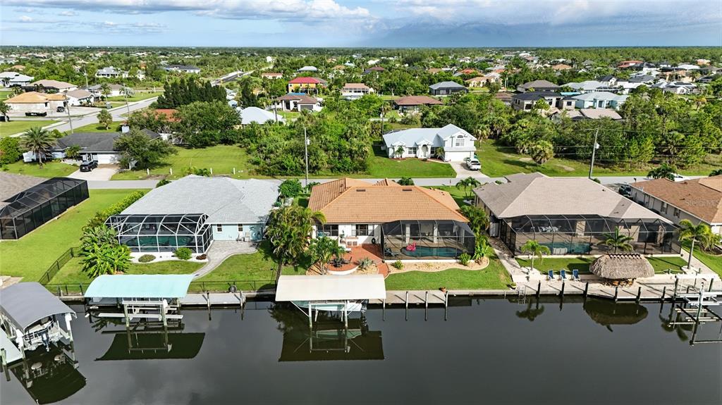 An aerial view shows three waterfront houses with screened-in pools along a canal — 9402 MIGUE CIRCLE, PORT CHARLOTTE, FL