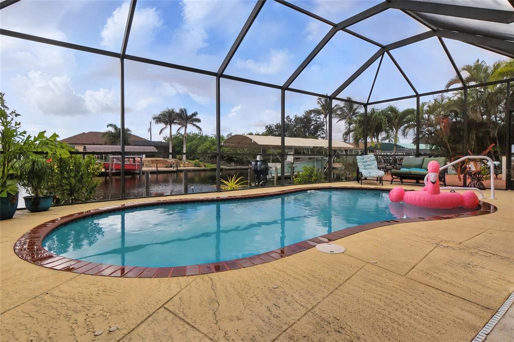 A screened-in swimming pool with a brick border overlooks a canal with boat docks — 9402 MIGUE CIRCLE, PORT CHARLOTTE, FL