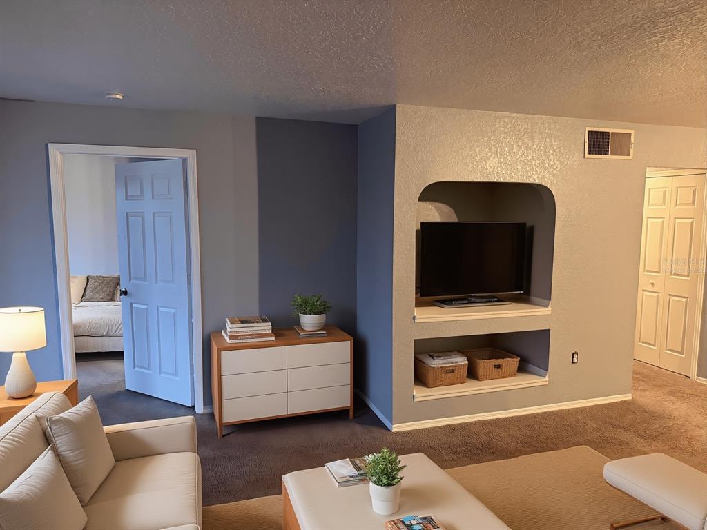 A living room features a built-in media niche, a dresser, and a doorway to a bedroom — 13838 FAIRWAY ISLAND DRIVE UNIT 1432, ORLANDO, FL