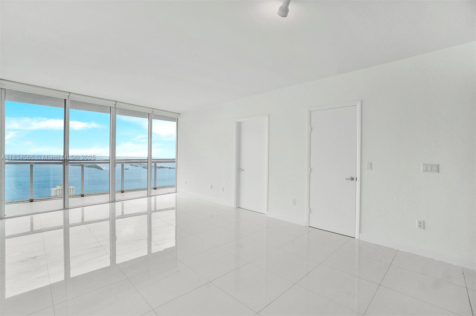 An empty room with white tile floors, two closed doors, and floor-to-ceiling windows overlooking water — 465 Brickell Ave # 4505, Miami FL 33131, MIAMI, FL
