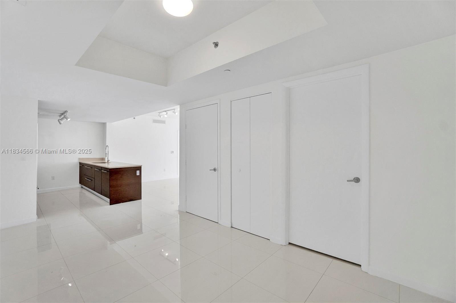 A bright, minimalist interior features white tile flooring, white walls, and a dark kitchen island — 465 Brickell Ave # 4505, Miami FL 33131, MIAMI, FL