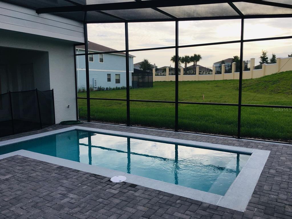 A rectangular swimming pool with a stone deck is enclosed by a screened-in lanai — 2452 DUBAI ST, KISSIMMEE, FL