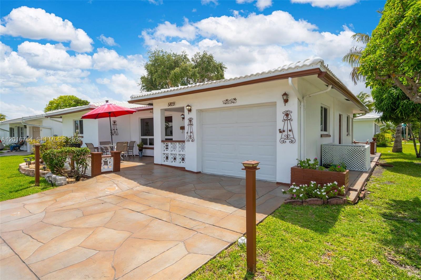 A single-story white house features a stone-patterned driveway, a garage, and a small patio — 5809 NW 83rd Ave, Tamarac FL 33321, TAMARAC, FL